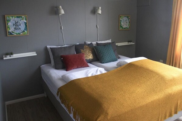A neatly made bed with a yellow throw blanket, multiple pillows in various colors, and two wall-mounted lamps.