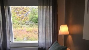 A hotel room with a bed, two pillows, a window with curtains, and a lamp. - Guesthouse Stekkaból (Vesturbyggð)