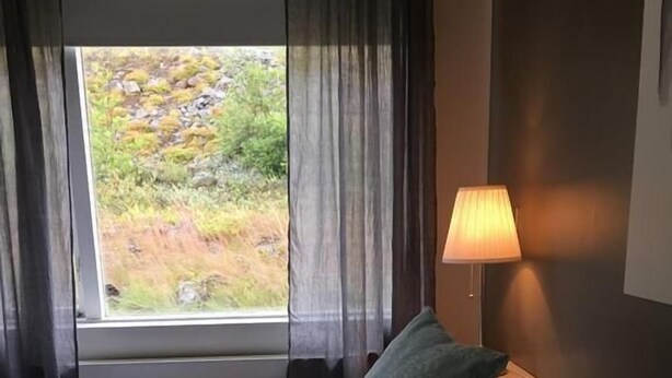 Une chambre d’hôtel avec un lit, deux oreillers, une fenêtre avec des rideaux et une lampe.