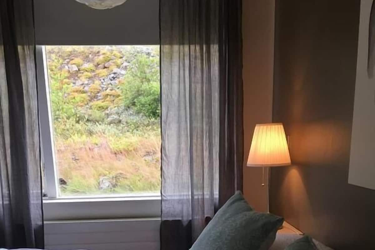 Habitación de hotel con cama, dos almohadas, ventana con cortinas y lámpara.