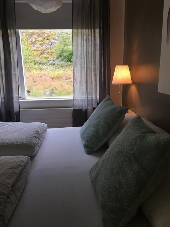 Une chambre d’hôtel avec un lit, deux oreillers, une fenêtre avec des rideaux et une lampe.