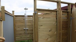 A wooden outdoor shower enclosure with a metal showerhead, a metal gate, and a metal chain lock. - Guesthouse Stekkaból (Vesturbyggð)