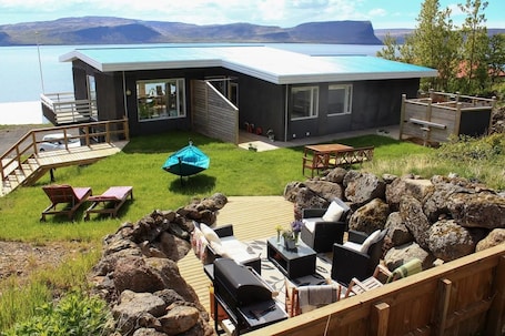A modern house with a deck, outdoor seating, and a view of the water.