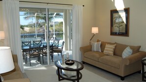 Ein Wohnzimmer mit einer Couch, einem Glastisch und Blick auf einen Pool sowie Gartenmöbel durch eine Glasschiebetür.