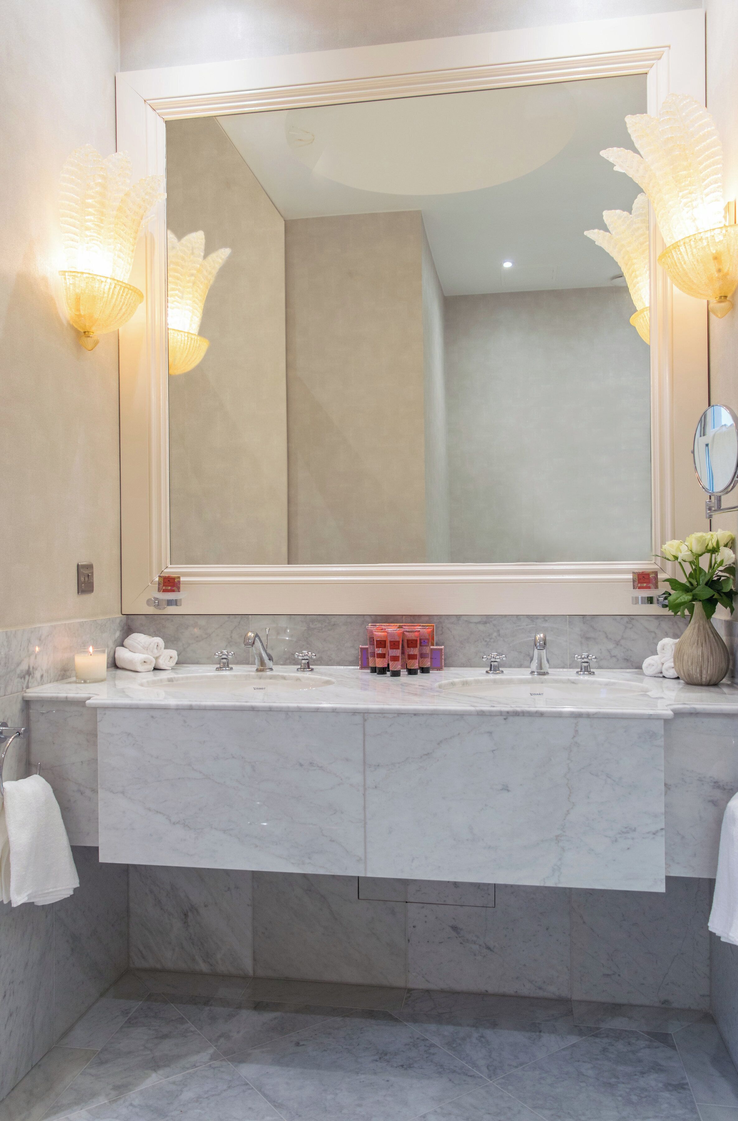 A bathroom with a large mirror, two sinks, and a vase with flowers.