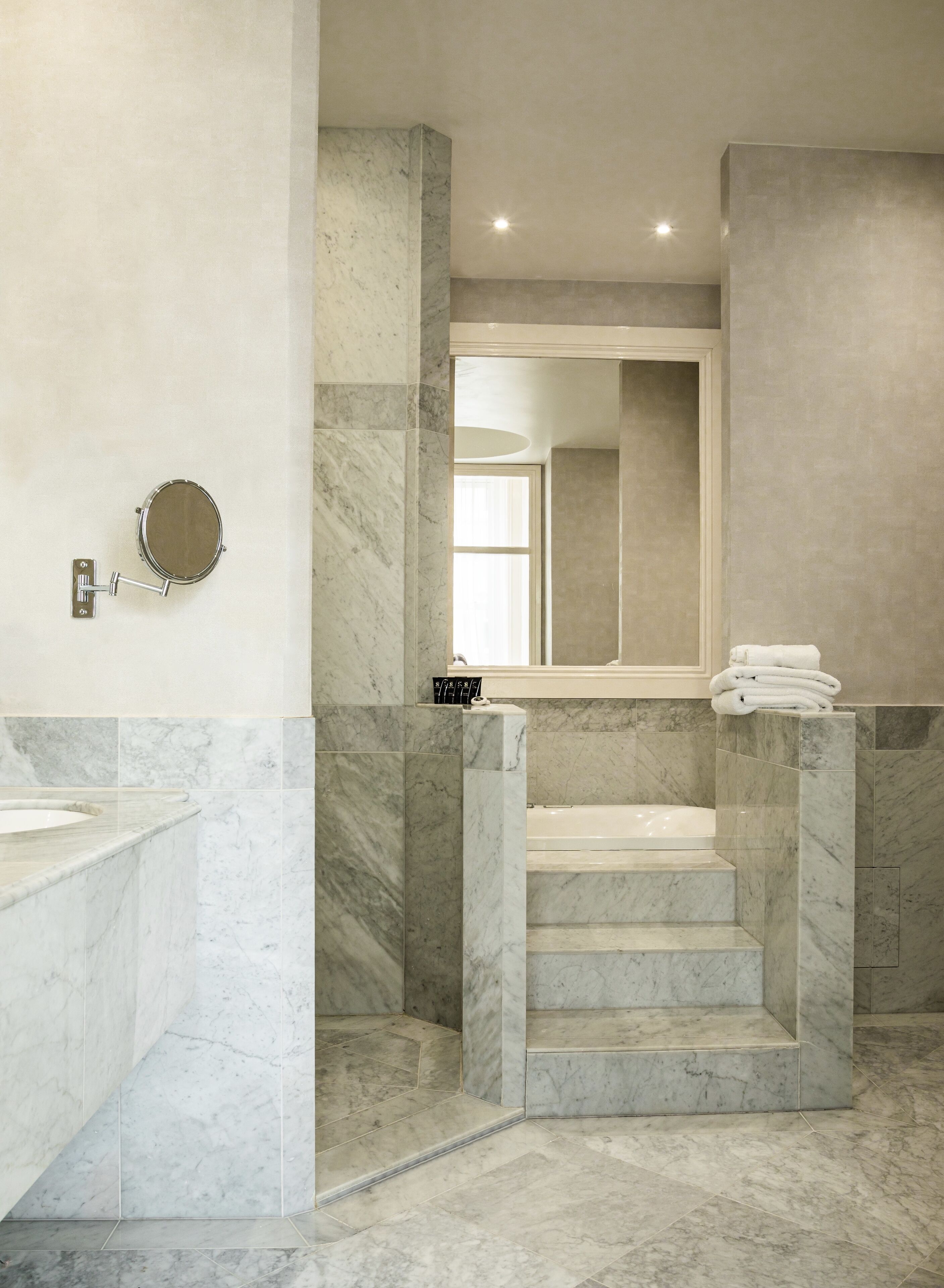 A modern bathroom with marble flooring, a large mirror, and a bathtub.