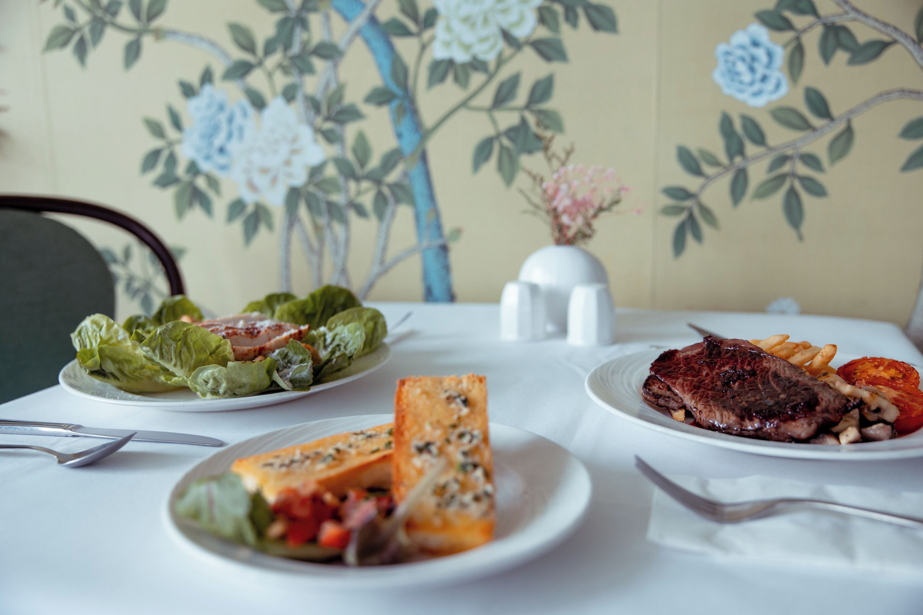 A dining table with plates of food, including steak, fries, and salad.