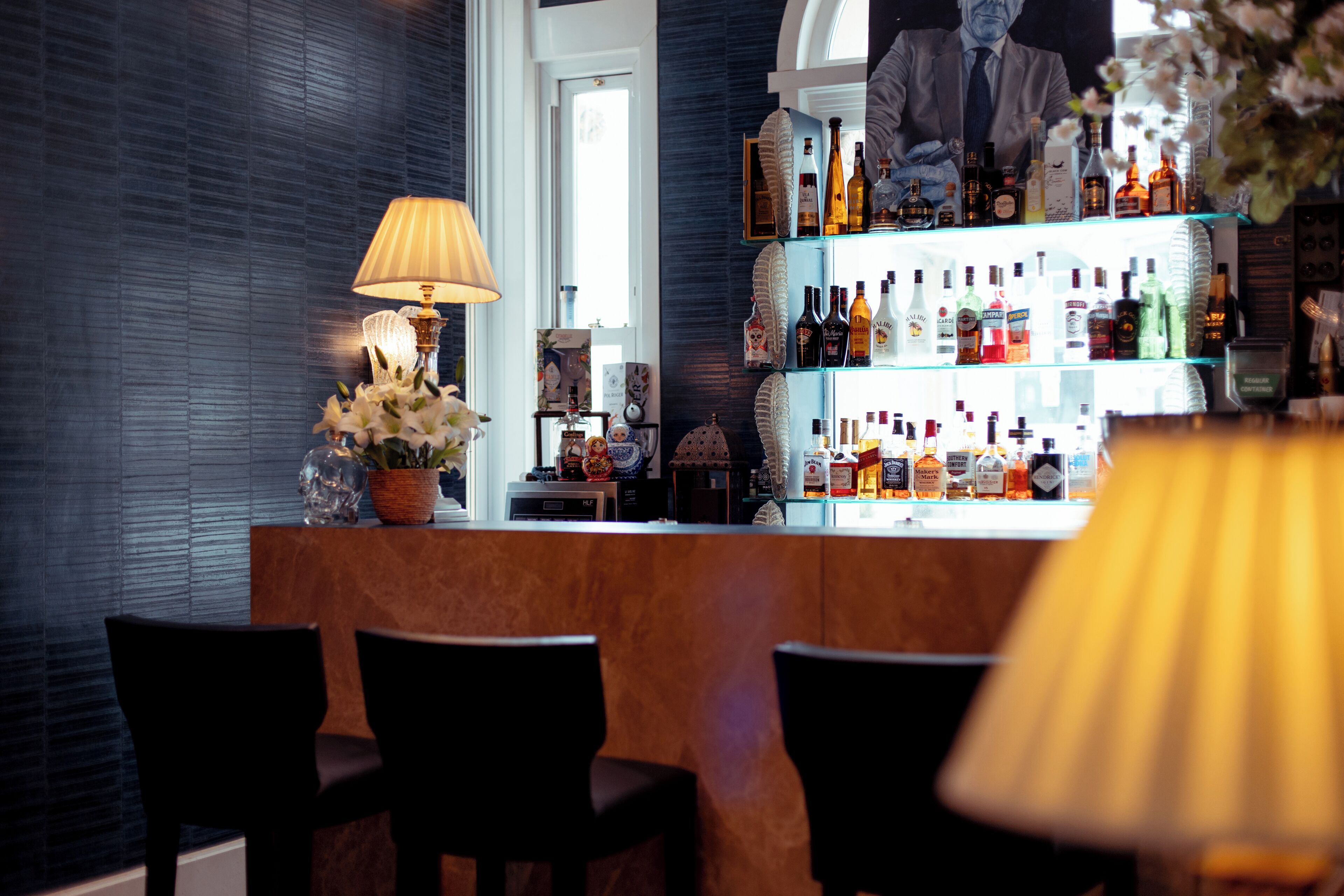 Un espace bar avec un comptoir en bois, une lampe et une étagère où sont exposées des bouteilles d’alcool.