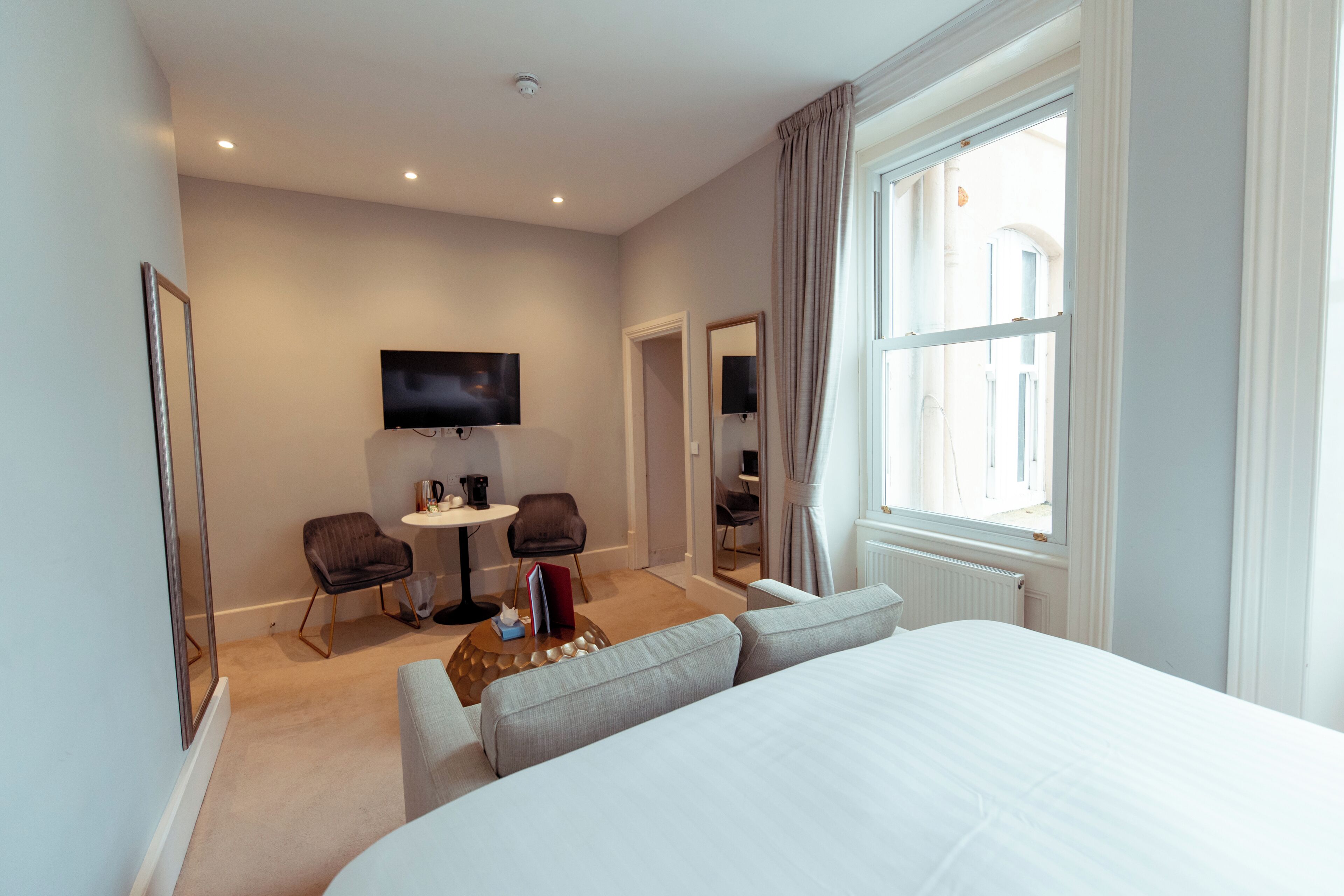 A hotel room with a bed, a TV, a desk with two chairs, and a window with curtains.