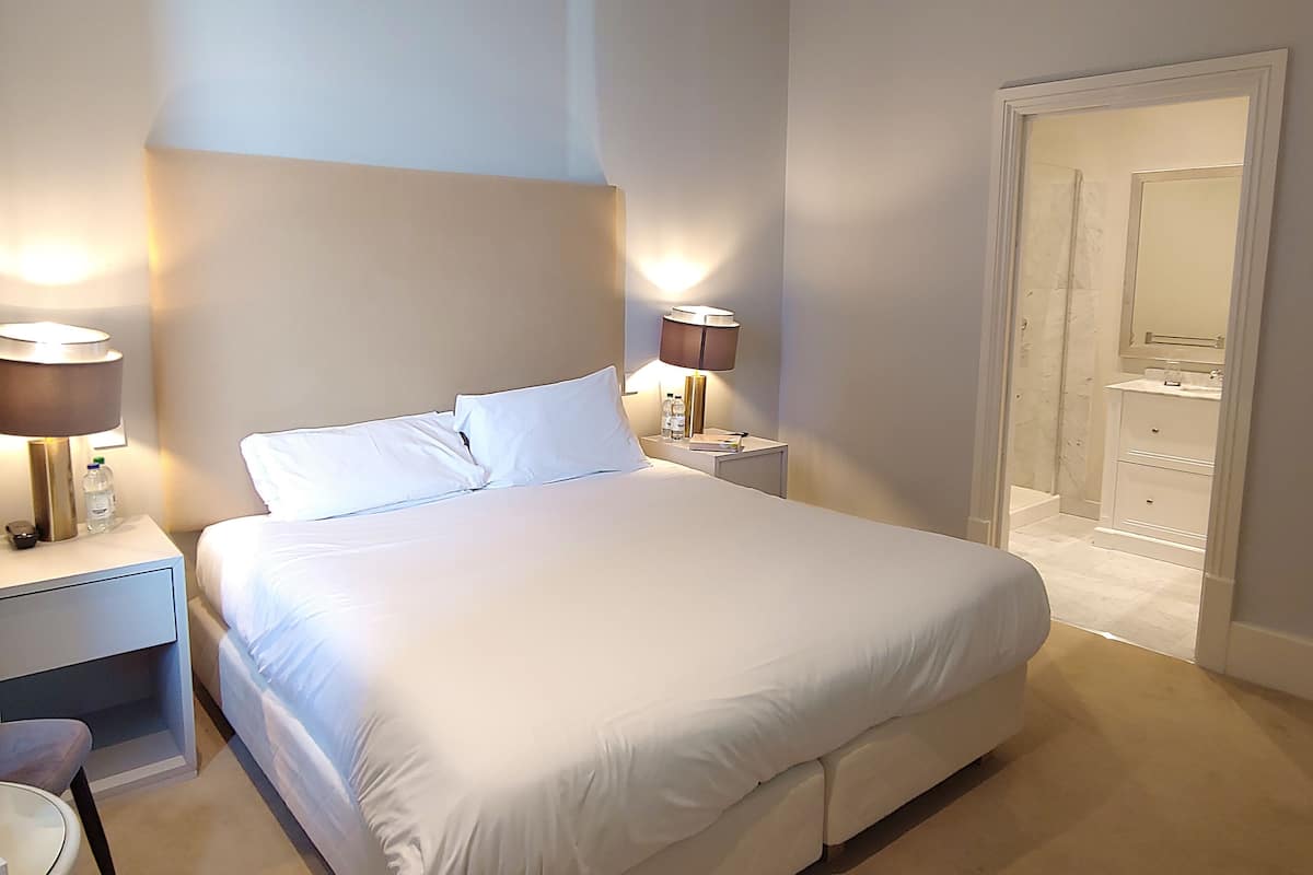 A modern hotel room with a large bed, bedside lamps, a small table, and a walk-in closet.