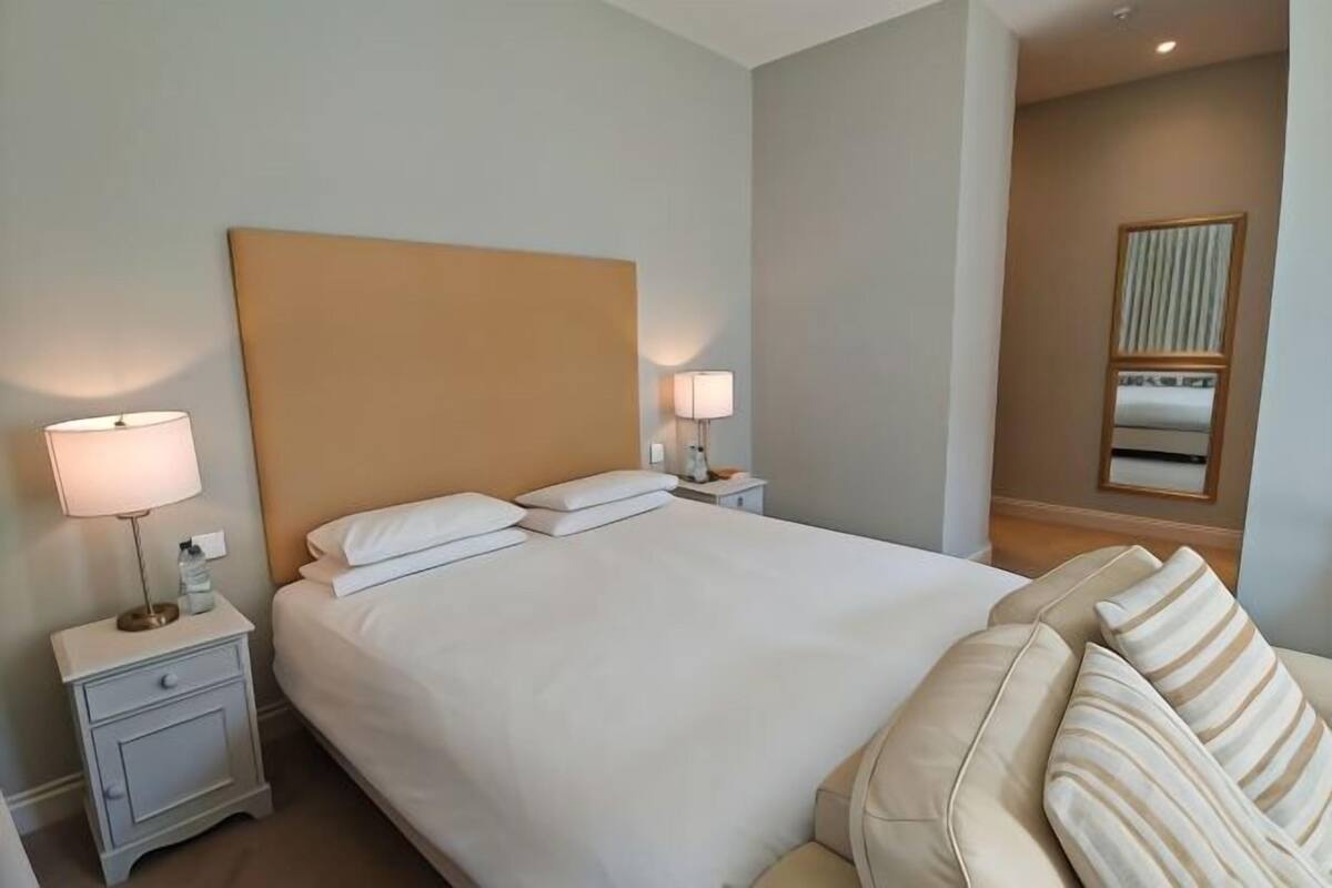 A hotel room with a large bed, two bedside tables with lamps, a mirror, and a sofa.