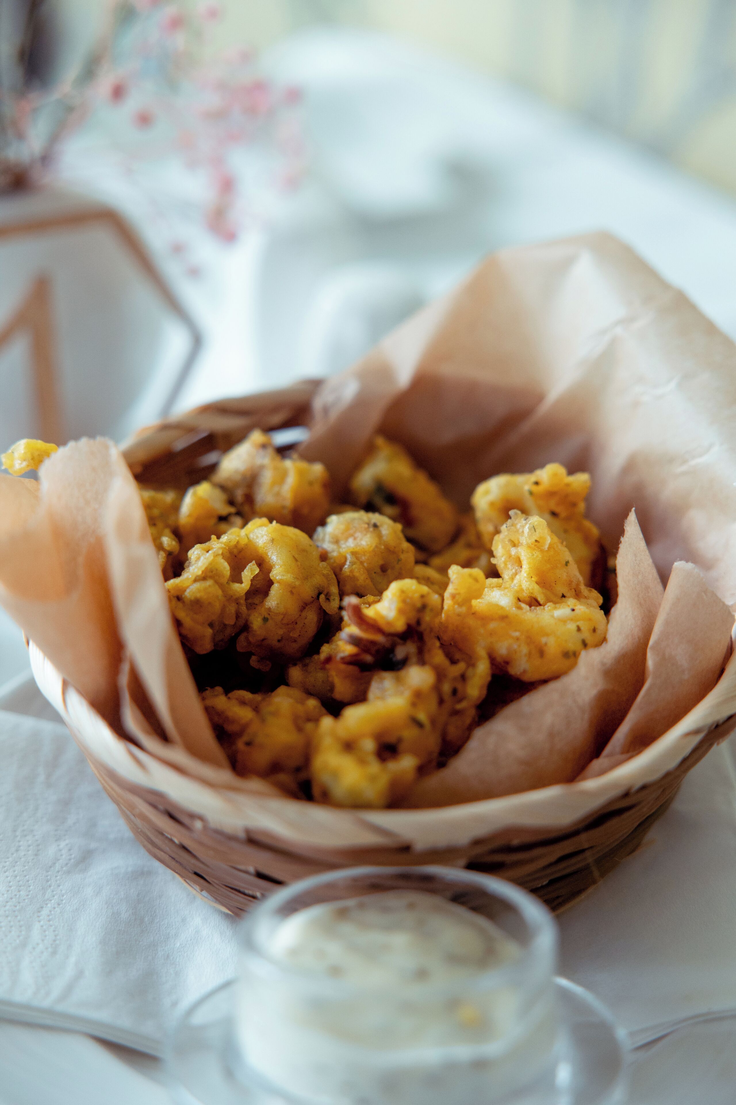 A basket of fried food items on a table with a napkin and a small container of sauce.