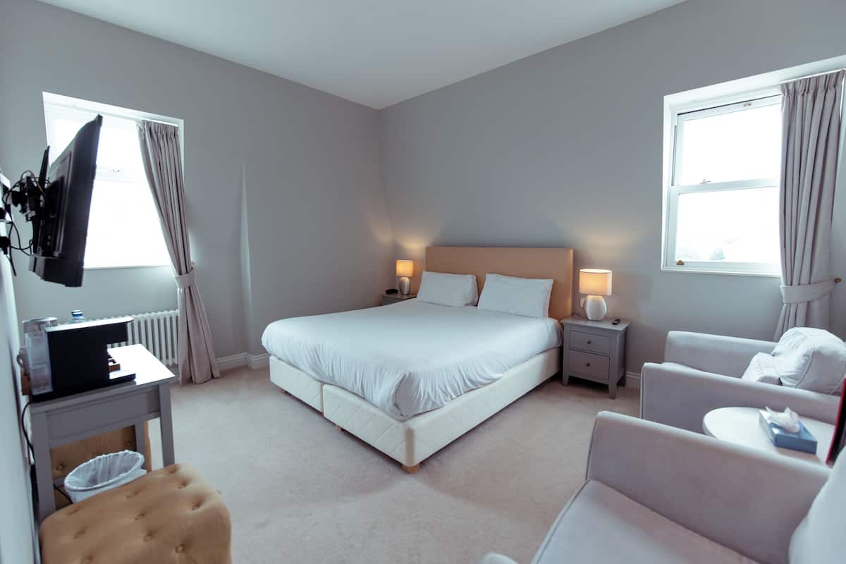 A hotel room with a large bed, bedside tables, a desk, a chair, and a TV.