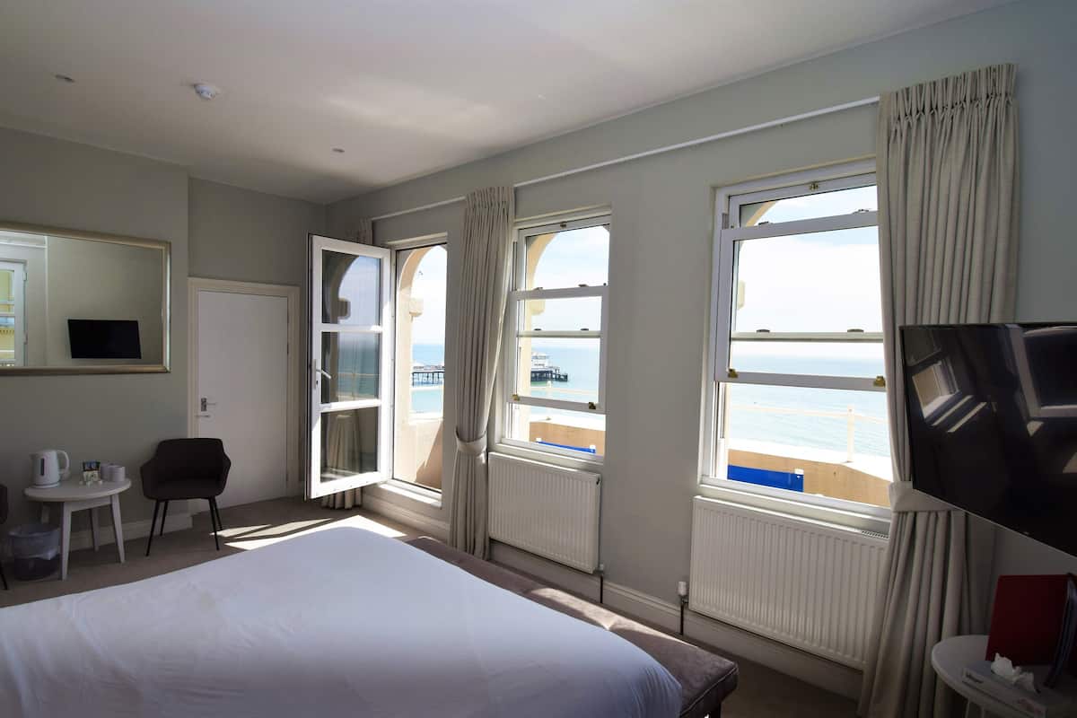A hotel room with a bed, a desk with a chair, a TV, and large windows with curtains.