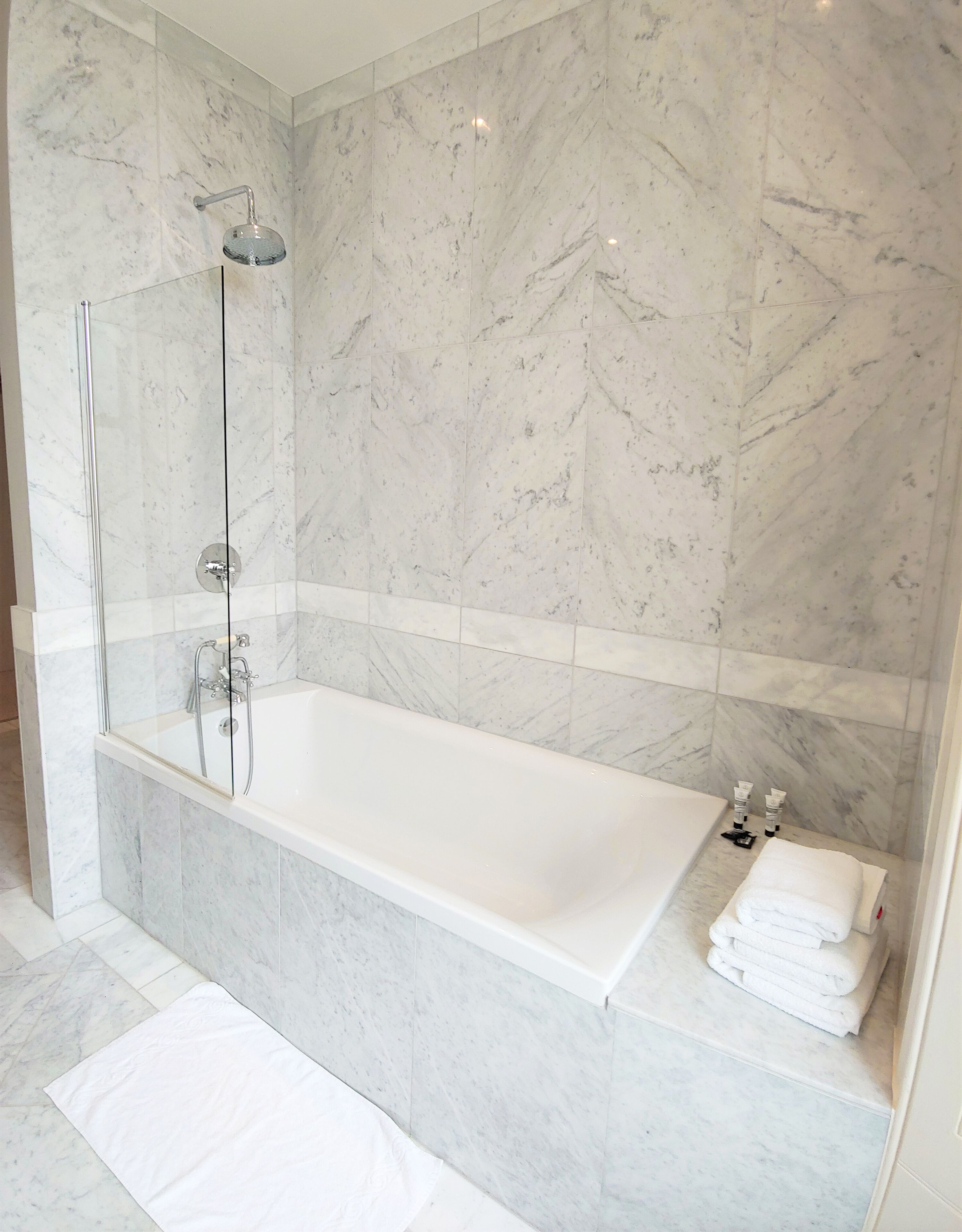 Un baño moderno con una bañera amplia, ducha con mampara de vidrio y paredes de mármol.