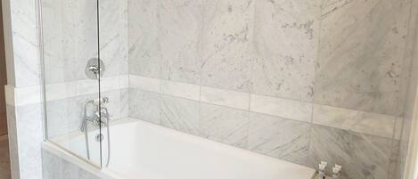 Un baño moderno con una bañera amplia, ducha con mampara de vidrio y paredes de mármol.