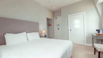 A hotel room with a large bed, a bedside table with a lamp, a desk with a chair, and a wardrobe.