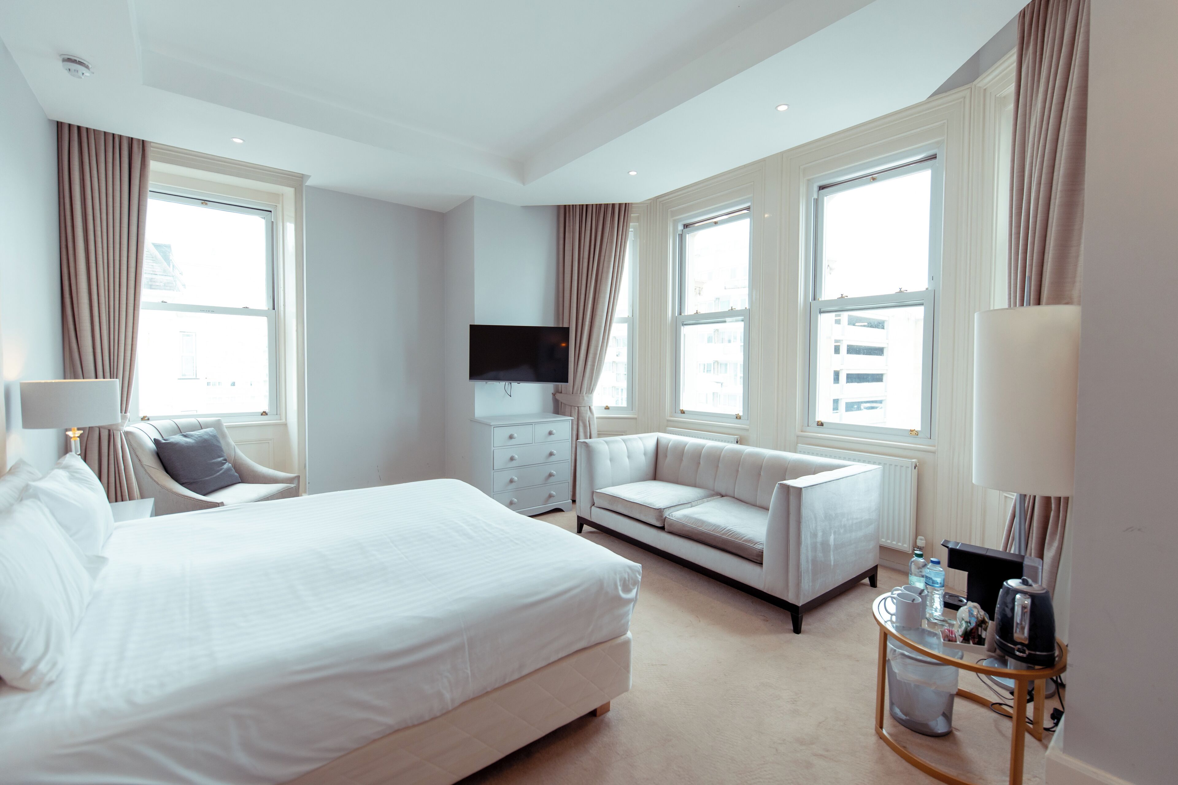 Habitación de hotel con una cama grande, un sofá, un televisor y una mesa de centro con artículos de cortesía.