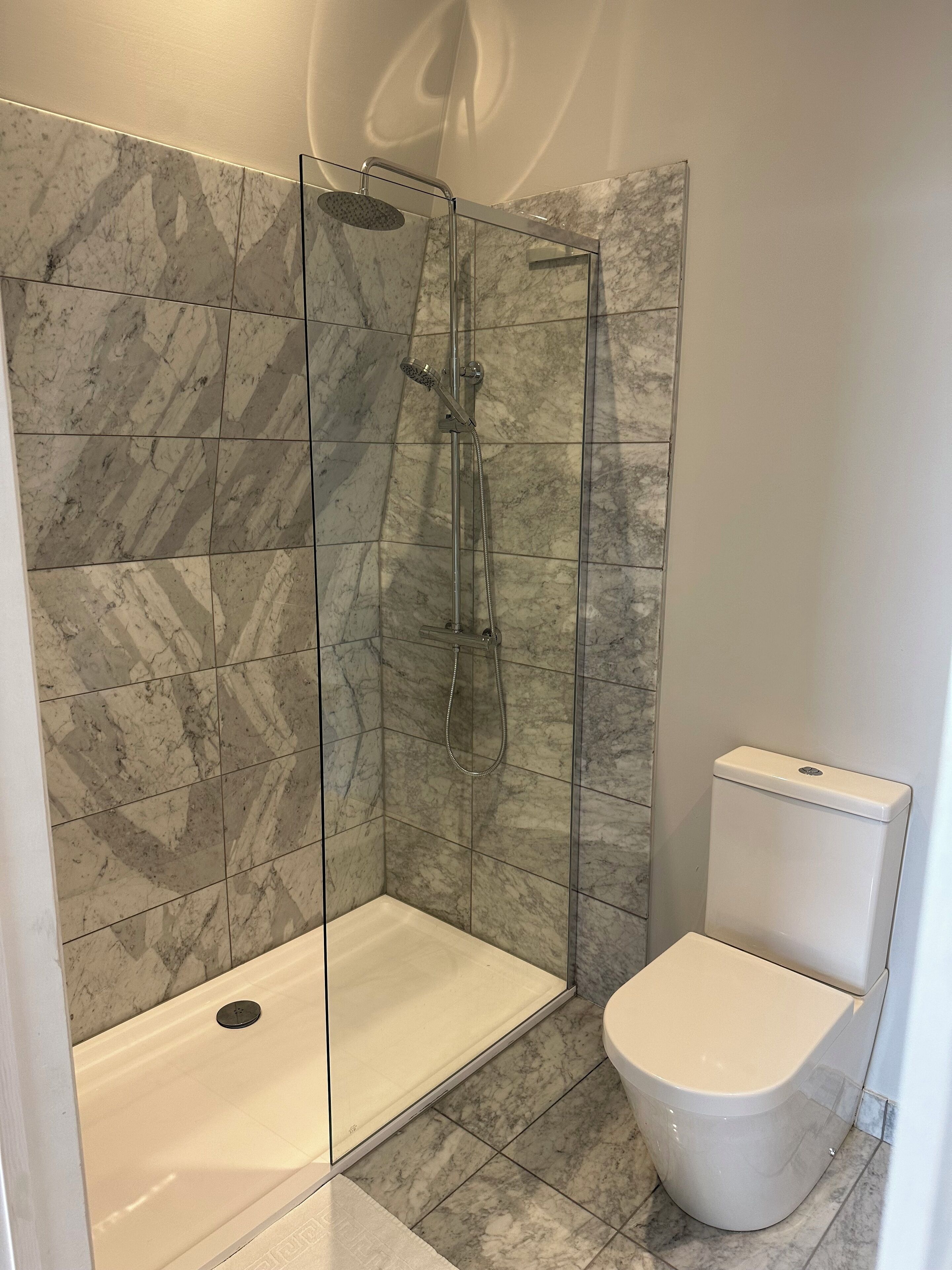Un baño moderno con ducha envuelta en vidrio, inodoro blanco y baldosas de mármol.