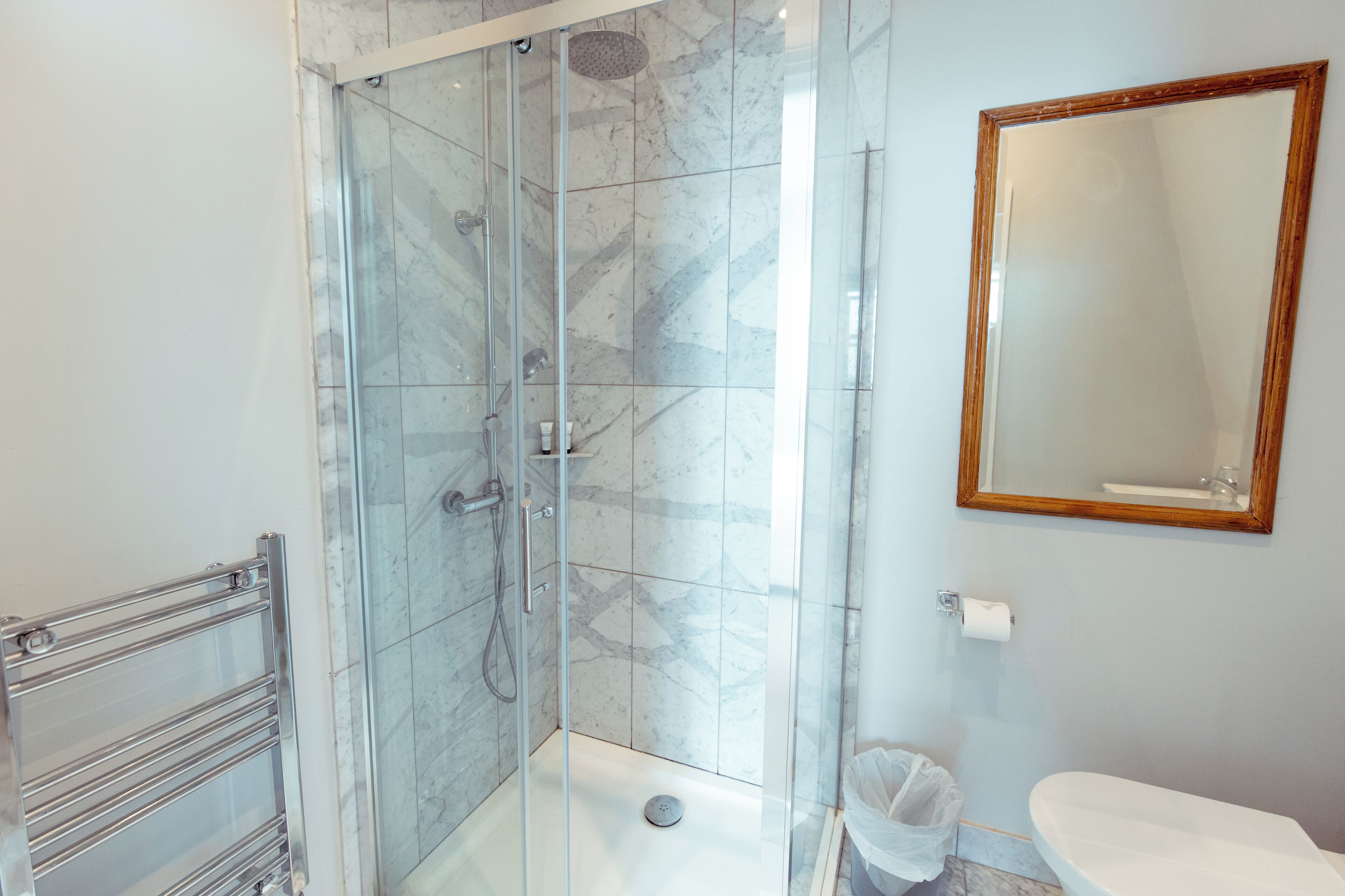 A modern bathroom with a glass-enclosed shower, a white toilet, and a marble-tiled floor.
