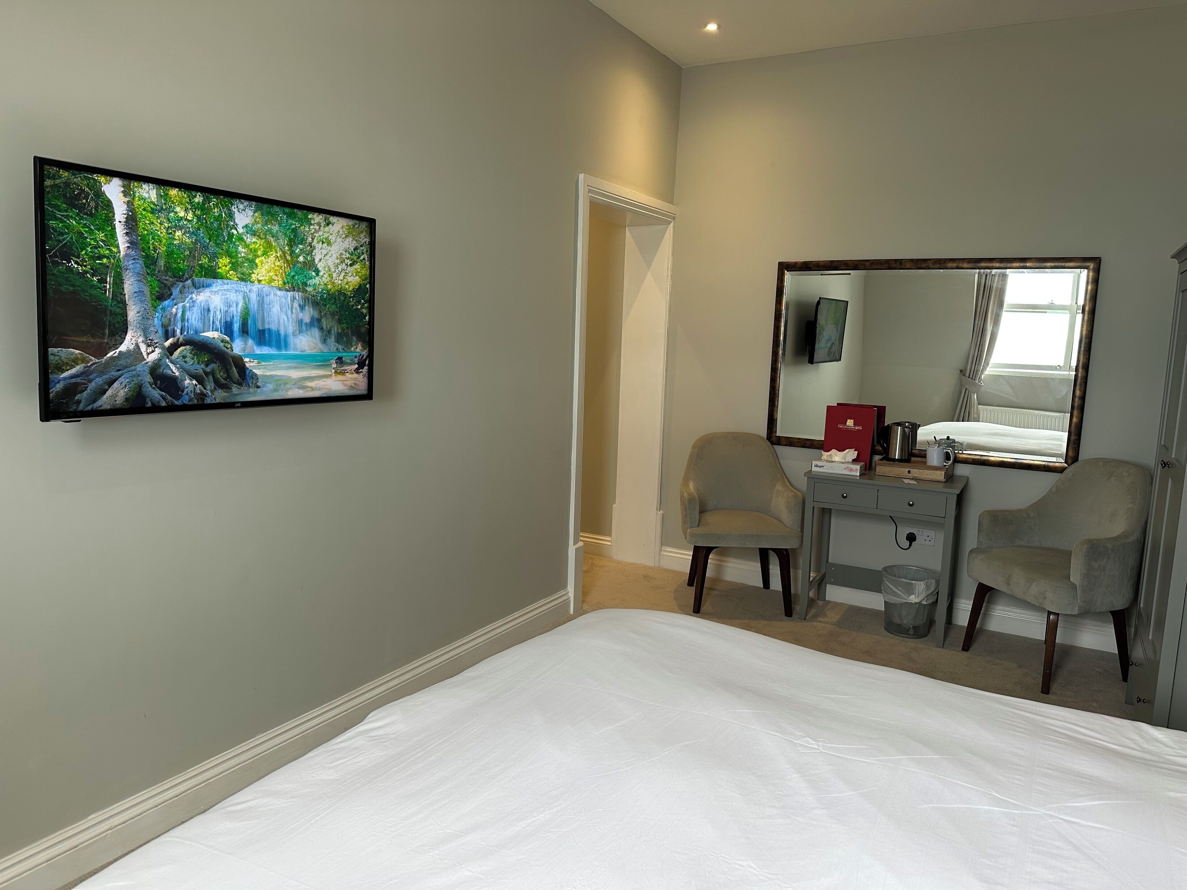 Habitación de hotel con una cama, un escritorio con dos sillas, un espejo grande y un cuadro de una cascada.