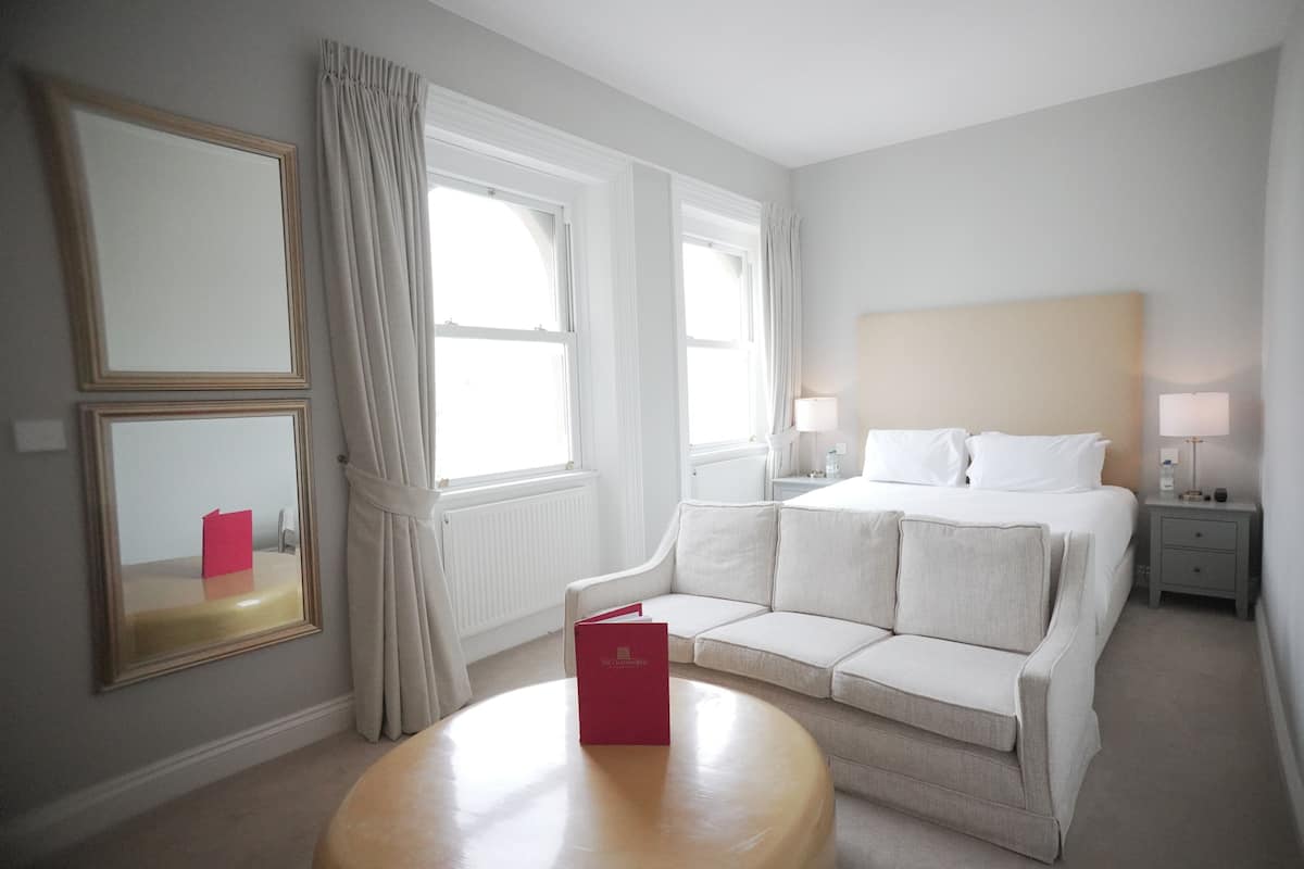A hotel room with a bed, a sofa, a round table, a nightstand, and a mirror.