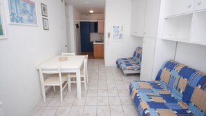 Un espace de vie compact comprenant une table à manger, des chaises, un canapé à motifs et, au fond, une petite cuisine.