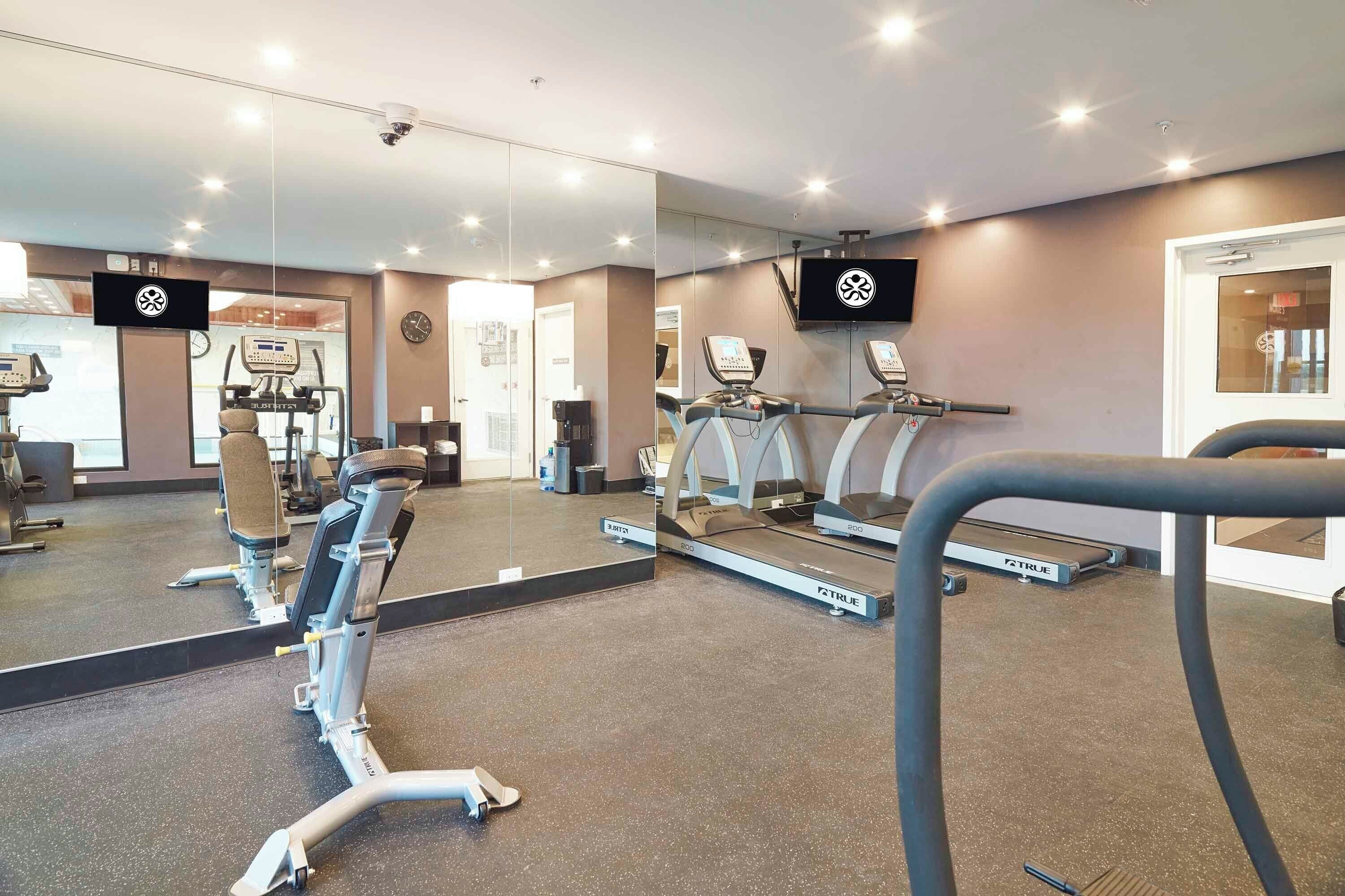 A gym with exercise equipment, mirrors, and a television.