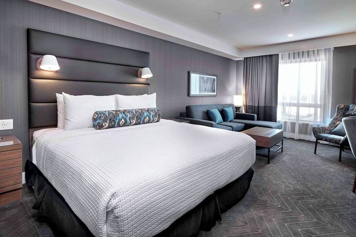 Ein modernes Hotelzimmer mit einem großen Bett, einem Schlafsofa, einem Sessel und einem Schreibtisch.