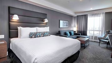 A modern hotel room with a large bed, a sofa, a chair, and a desk.