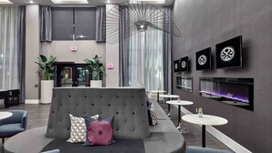 A modern lobby with a grey sofa, multiple seating areas, a fireplace, and a ceiling light fixture. - Sandman Signature Plano - Frisco Hotel (Plano)