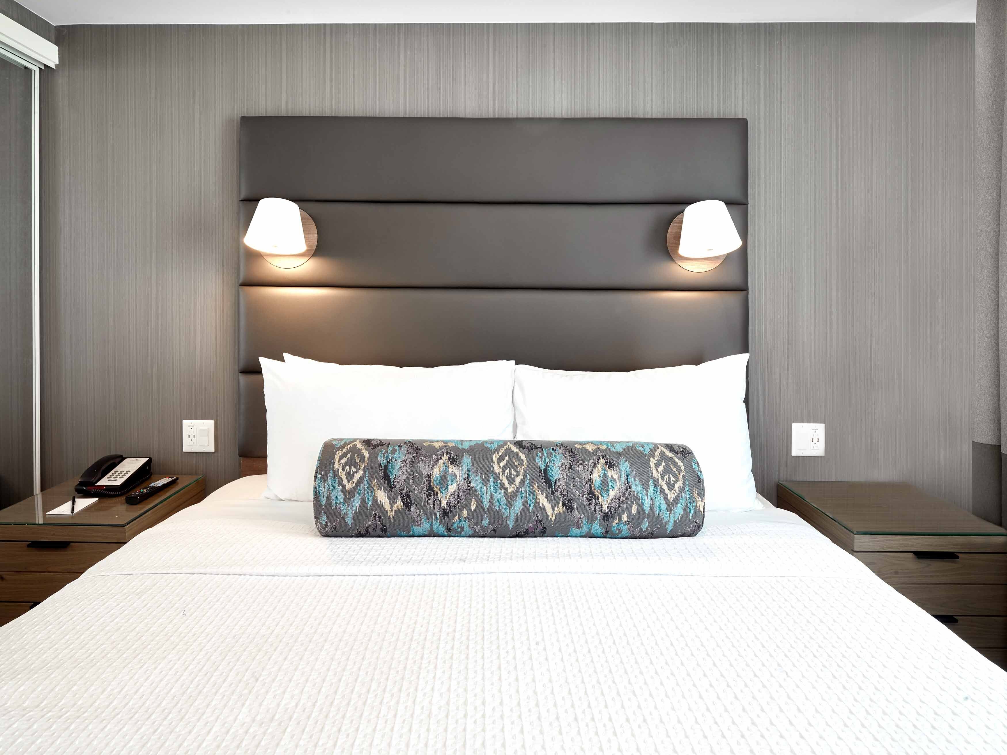 A hotel room with a large bed, two bedside lamps, a phone, and a nightstand.