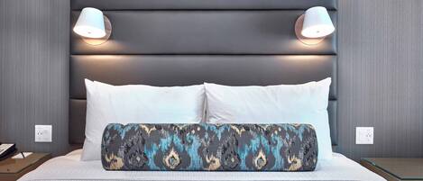 A modern hotel room with a large bed, two bedside lamps, and a patterned throw pillow.