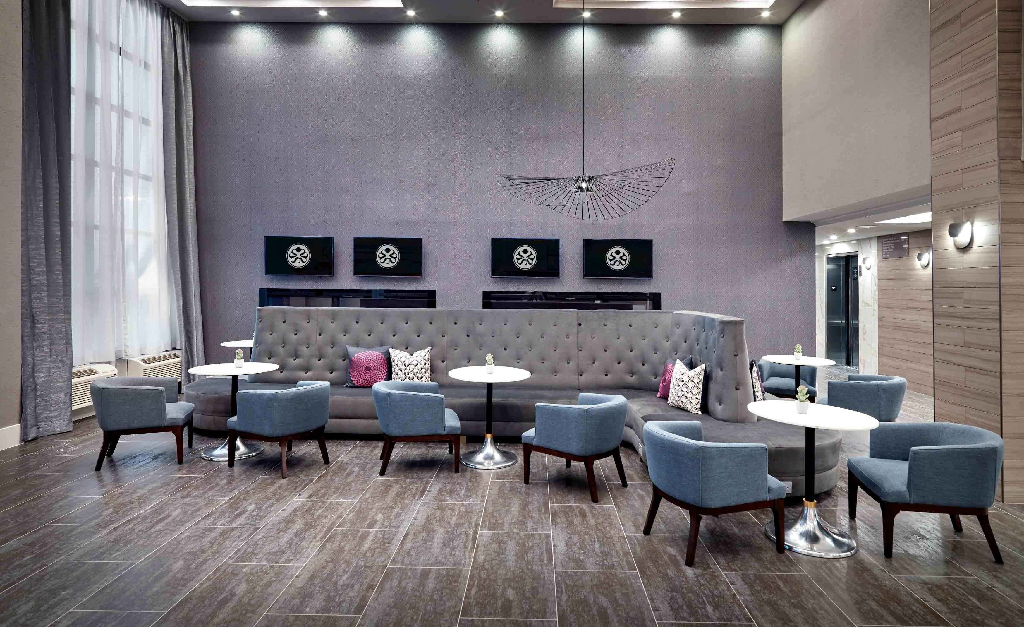 Un área de estar moderna con un sofá gris, sillones azules y pequeñas mesas redondas.