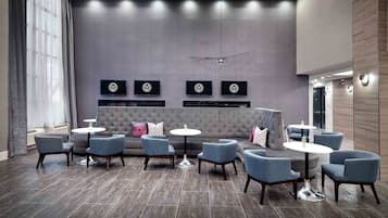 Un área de estar moderna con un sofá gris, sillones azules y pequeñas mesas redondas.