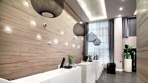 A modern reception area with a wooden wall, a marble reception desk, and pendant lighting. - Sandman Signature Plano - Frisco Hotel (Plano)