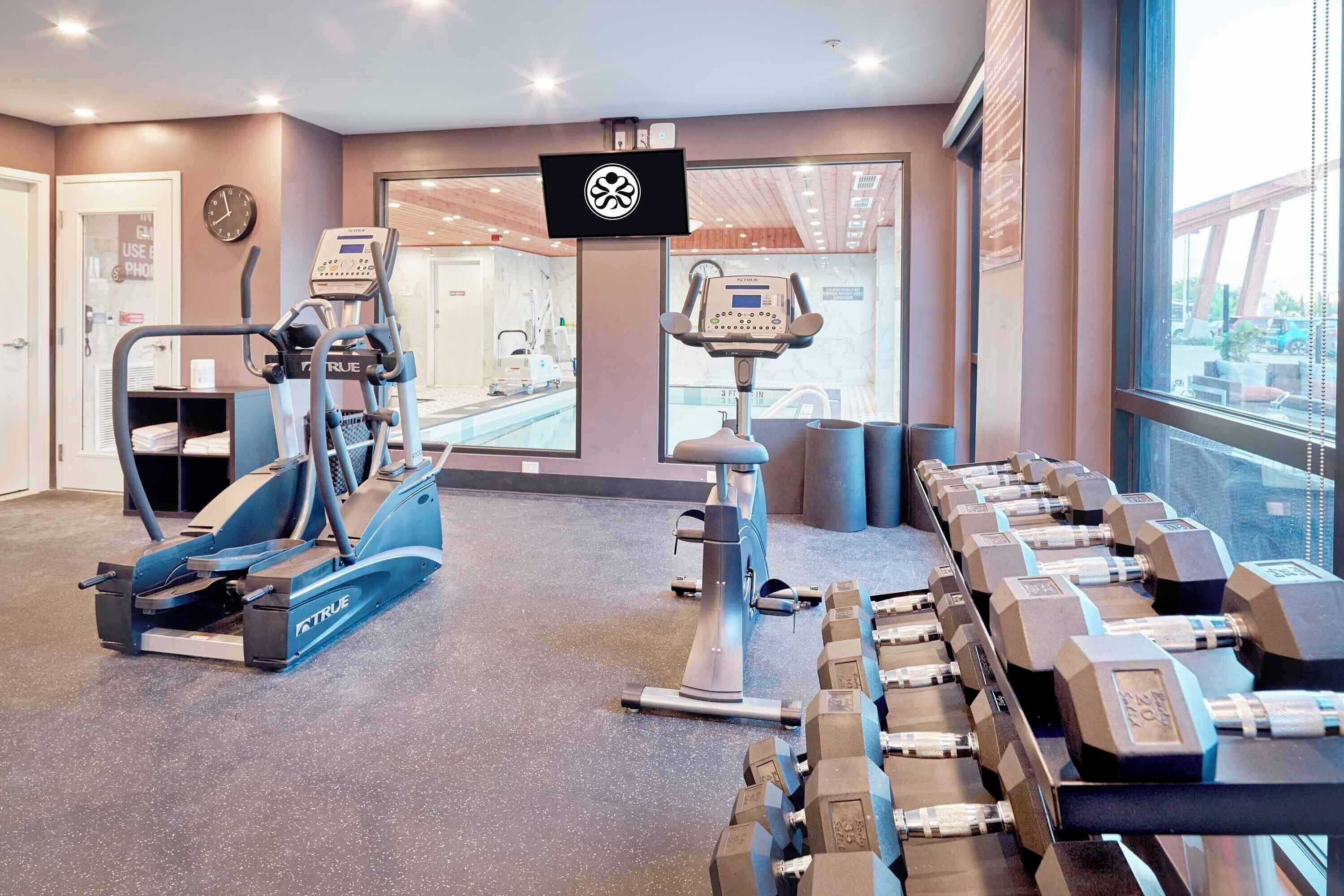 Et fitnessrum med løbebånd, vægte og et tv-skærm.