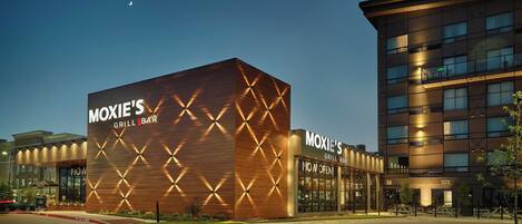 Un edificio moderno con el letrero 'MOXIE'S GRILL BAR', que presenta una fachada geométrica y una entrada visible.