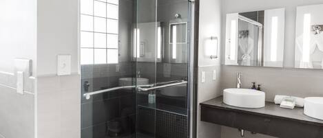 A modern bathroom with a glass-enclosed shower, a vanity with two sinks, and a large mirror above the vanity.
