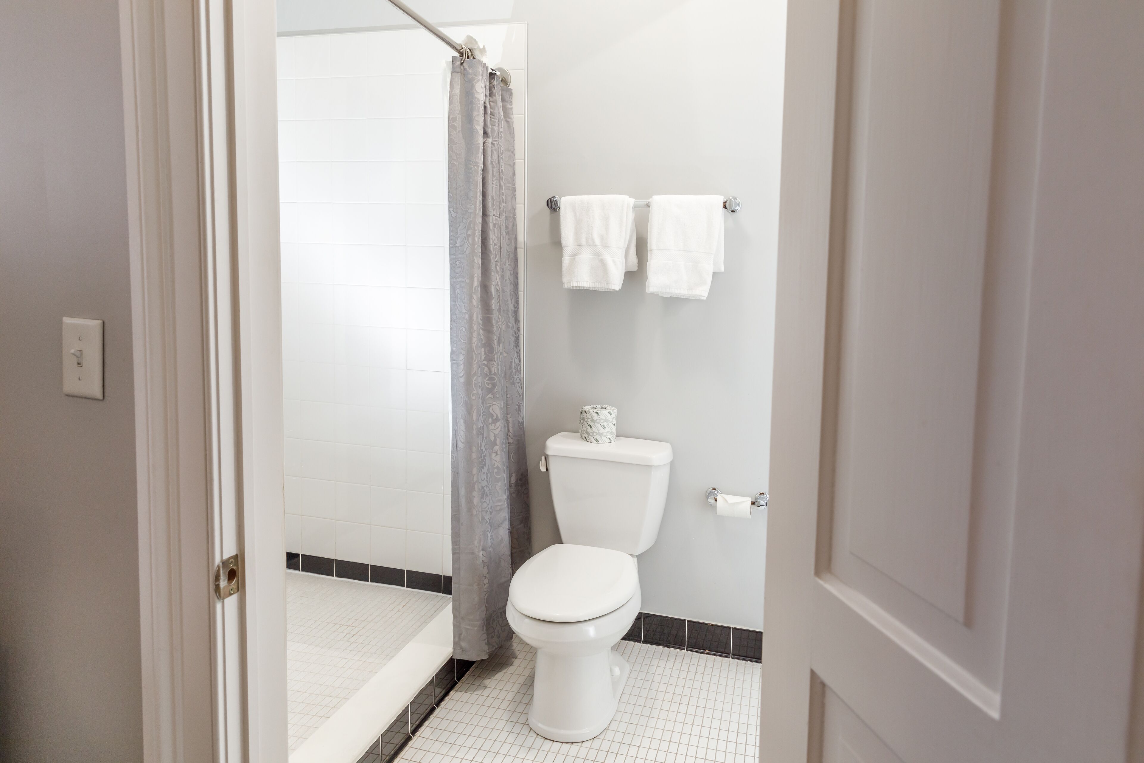 A bathroom with a white toilet, a shower curtain, and two white towels hanging on the wall.