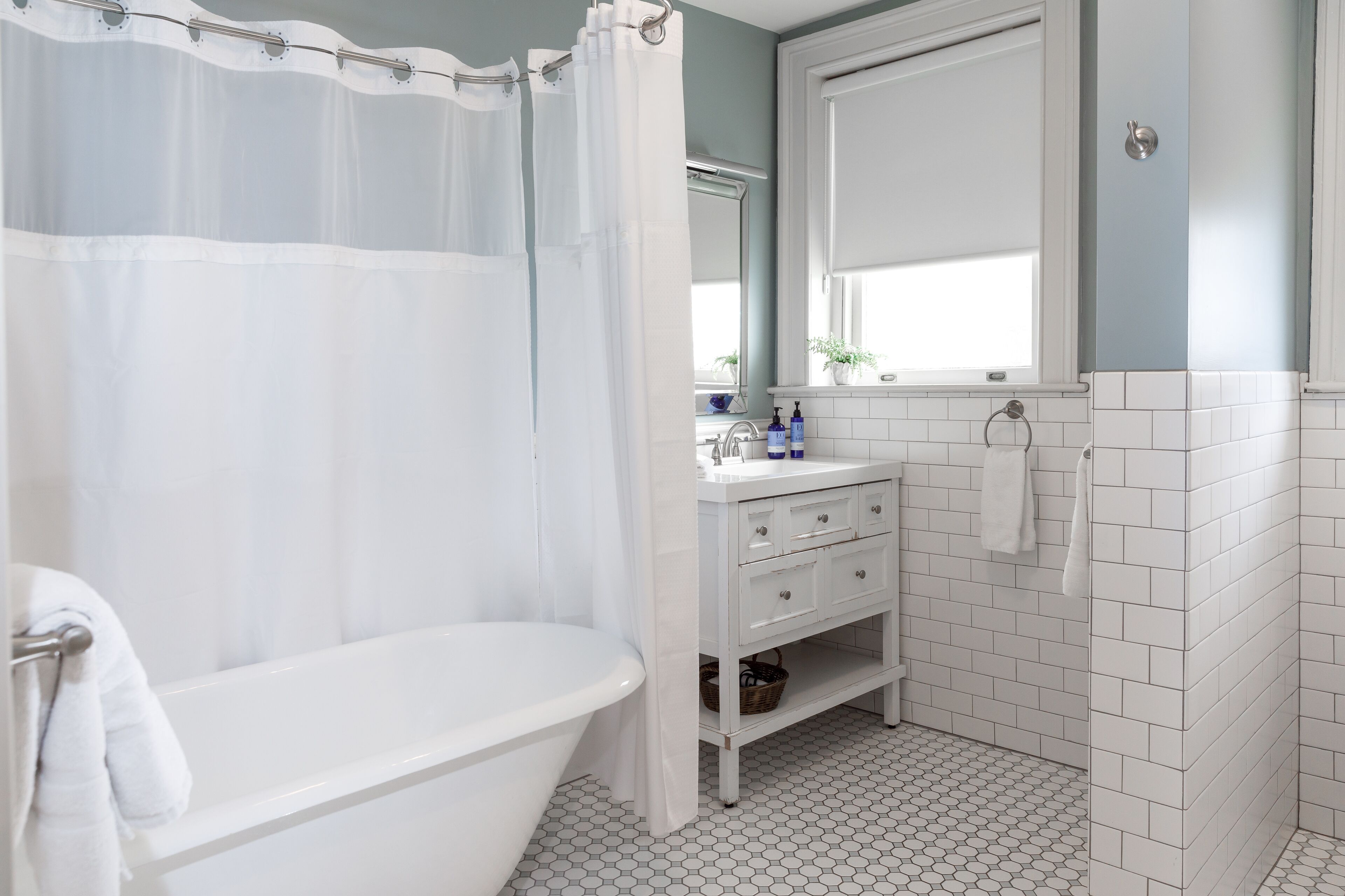 A bathroom with a bathtub, a shower curtain, a sink with toiletries, and a mirror.