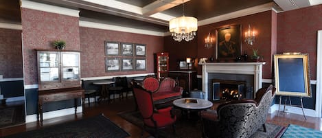 A traditional room with a fireplace, red upholstered chairs, a round table, and a chandelier.