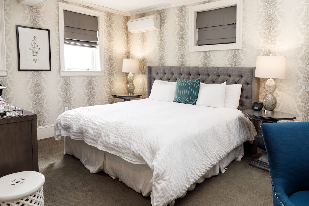 A neatly arranged hotel room with a large bed, two bedside tables with lamps, a small round table, and a blue chair.