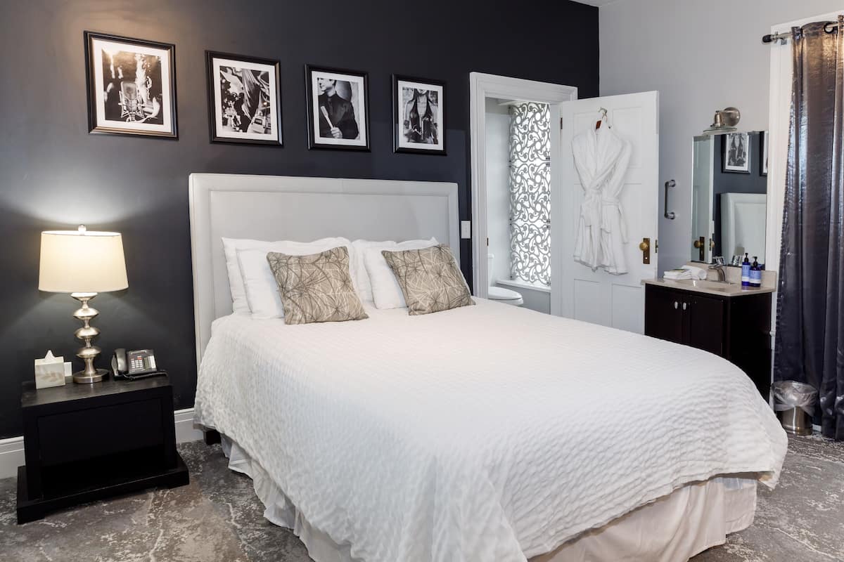 A neatly arranged bedroom with a large bed, a bedside table with a lamp, and a mirror above the sink.