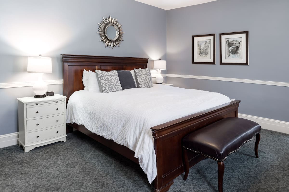 A neatly arranged bedroom with a large bed, two bedside tables, a bench, and a wall-mounted mirror.