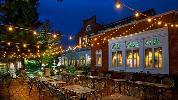 Un patio al aire libre con luces colgantes, edificios de ladrillo y mobiliario exterior.