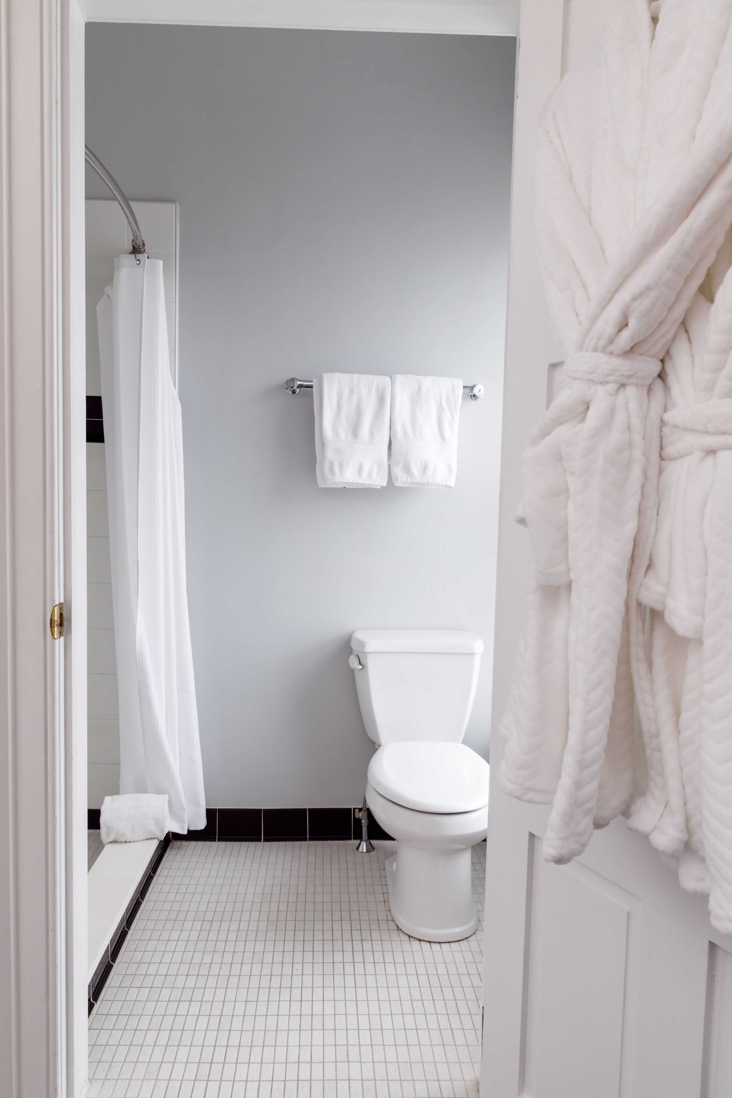 A bathroom with a white toilet, a white bathtub with a shower curtain, and a white towel rack with two towels.