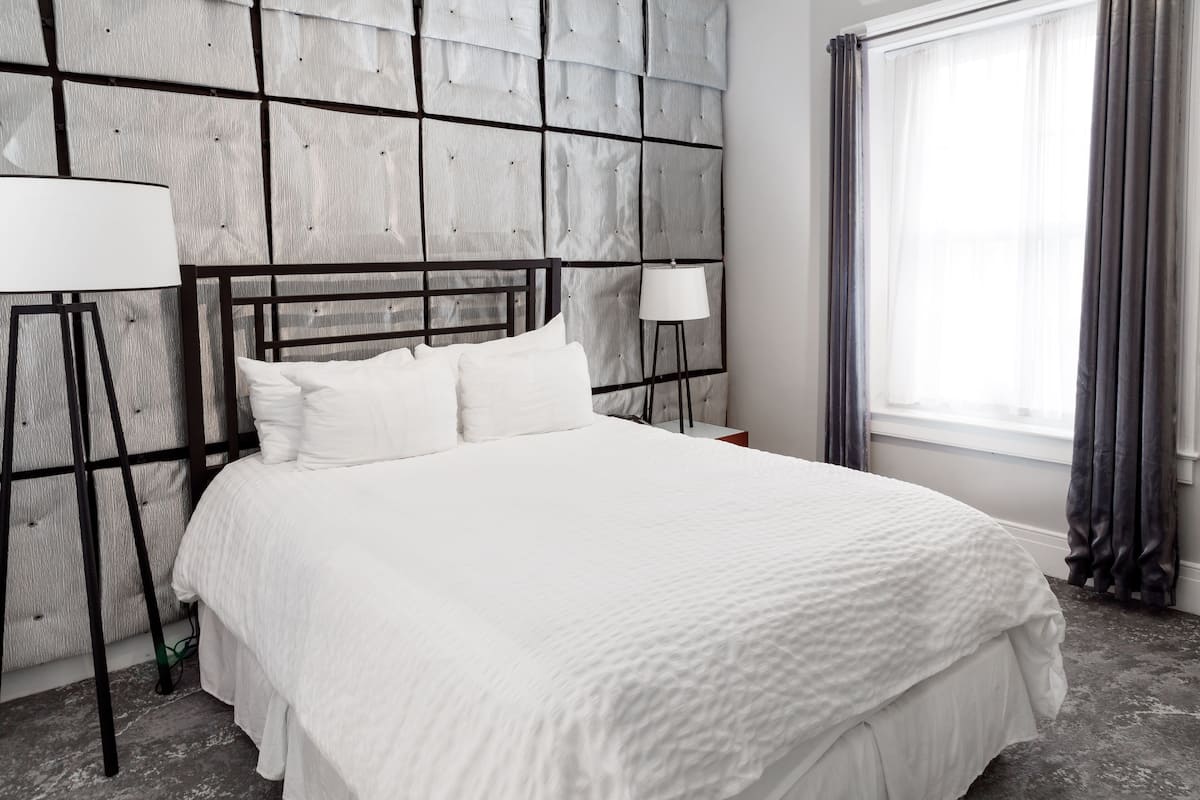 A neatly made bed with white bedding, a modern headboard, and two bedside lamps.