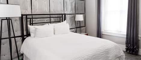 A neatly made bed with white bedding, a modern headboard, and two bedside lamps.