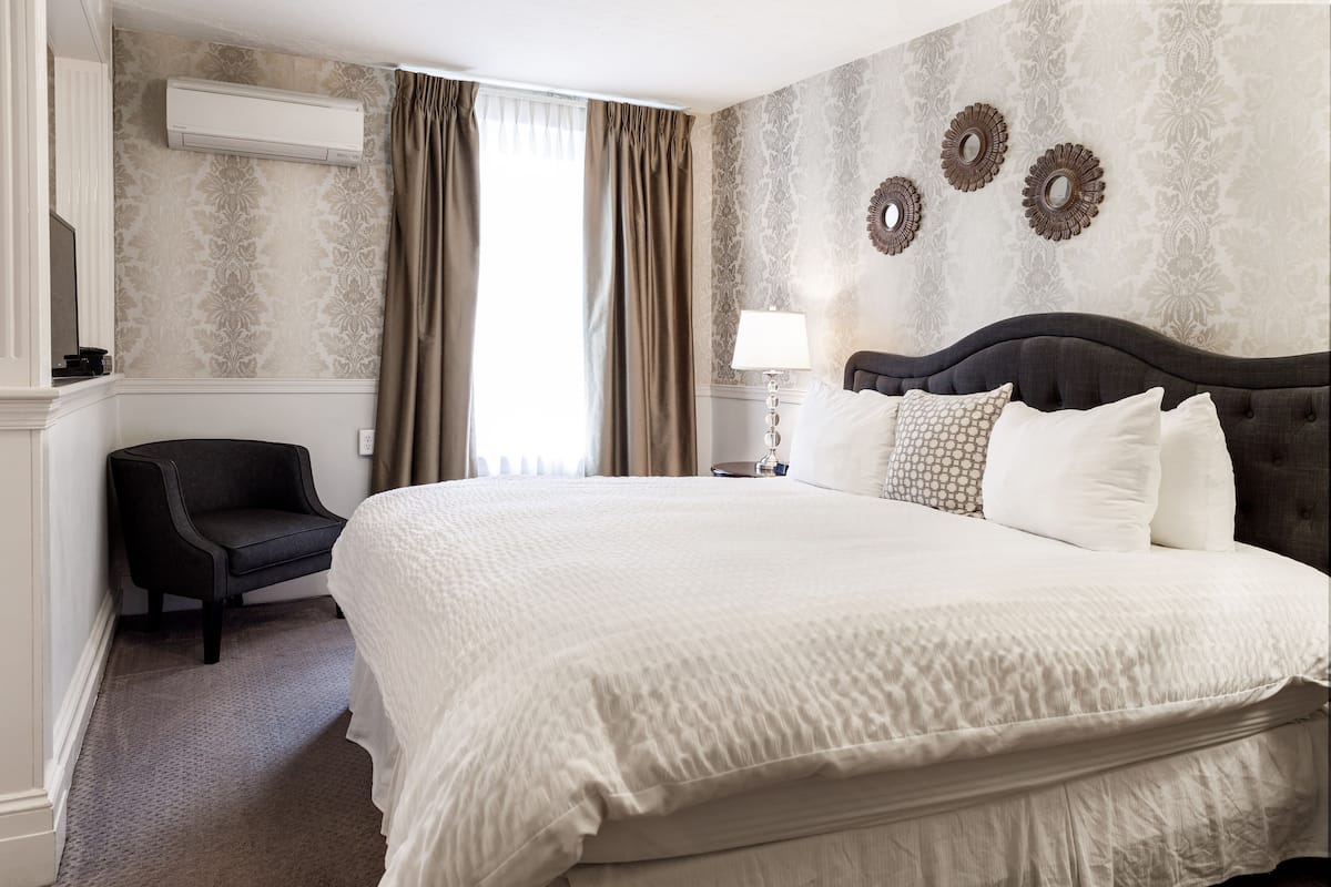 A hotel room with a large bed, a chair, a lamp, and decorative wall mirrors.